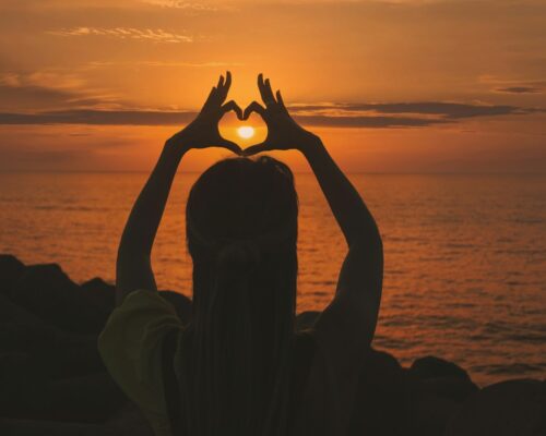silhouette of woman doing heart sign during sunset